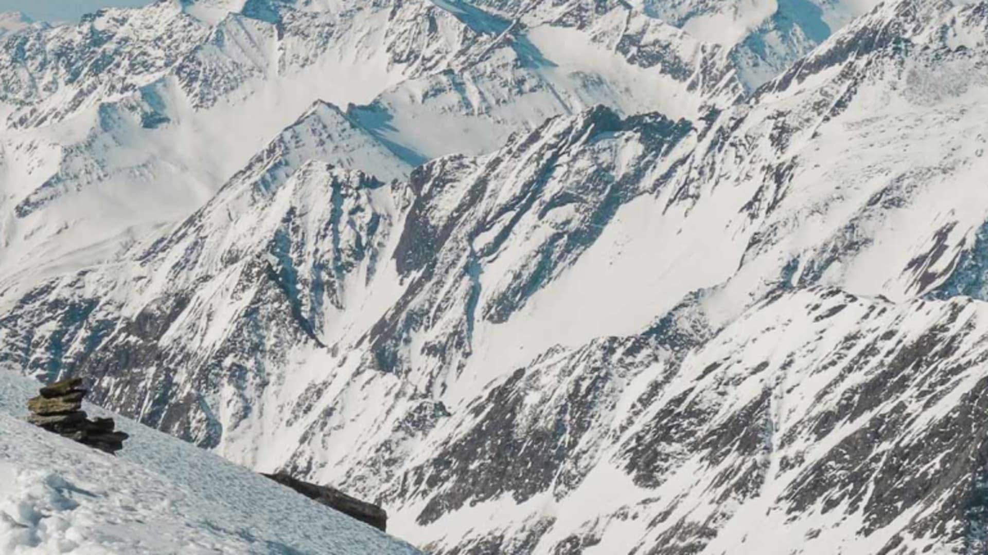 Schneeschuhwanderer mit Stock steht auf verschneitem Berggrat am Großvenediger mit Panorama der Hohen Tauern.