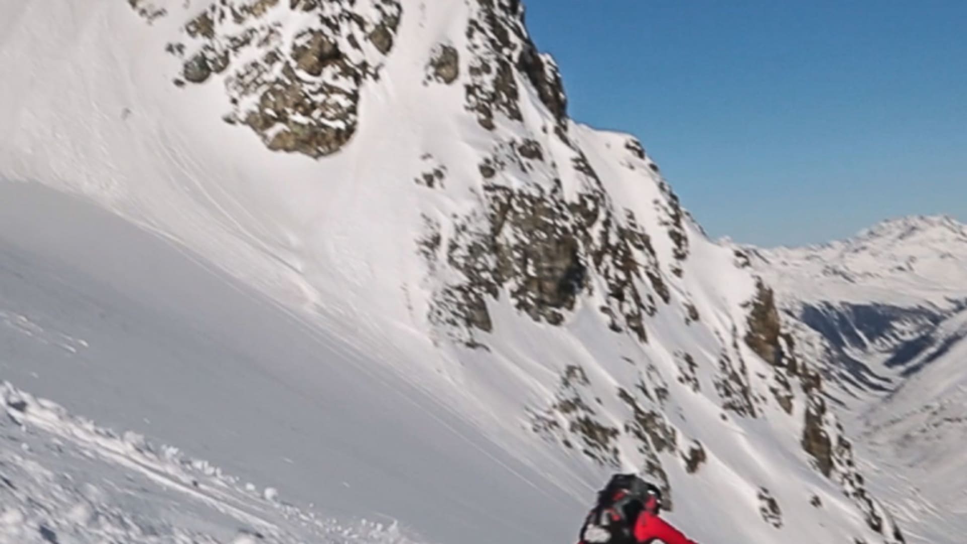 Ein Skitourengeher fährt mit aufgewirbeltem Pulverschnee einen steilen Hang von der Dreiländerspitze ab.