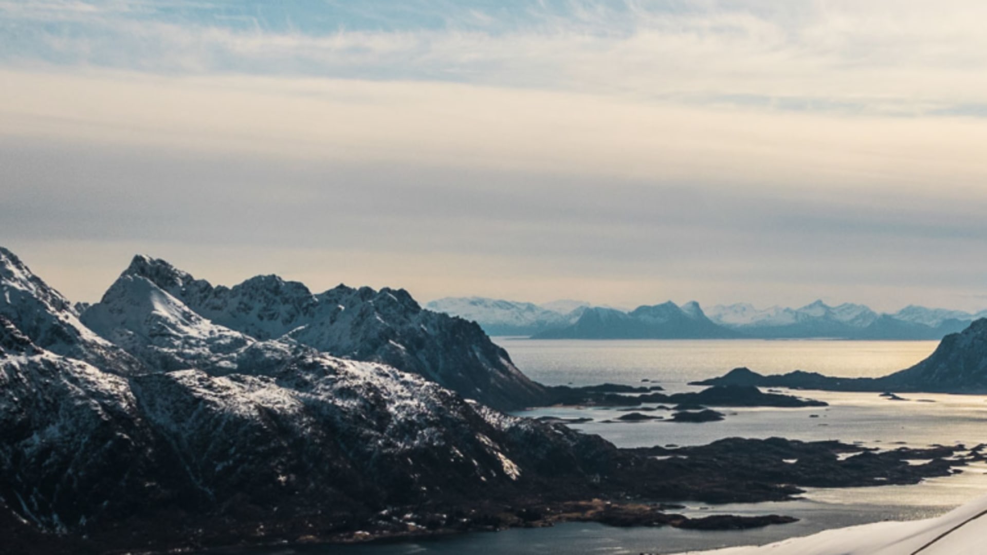 Skitourengeher in Abfahrtshaltung auf steilem Hang mit Fjord und Schären im Hintergrund auf den Lofoten.