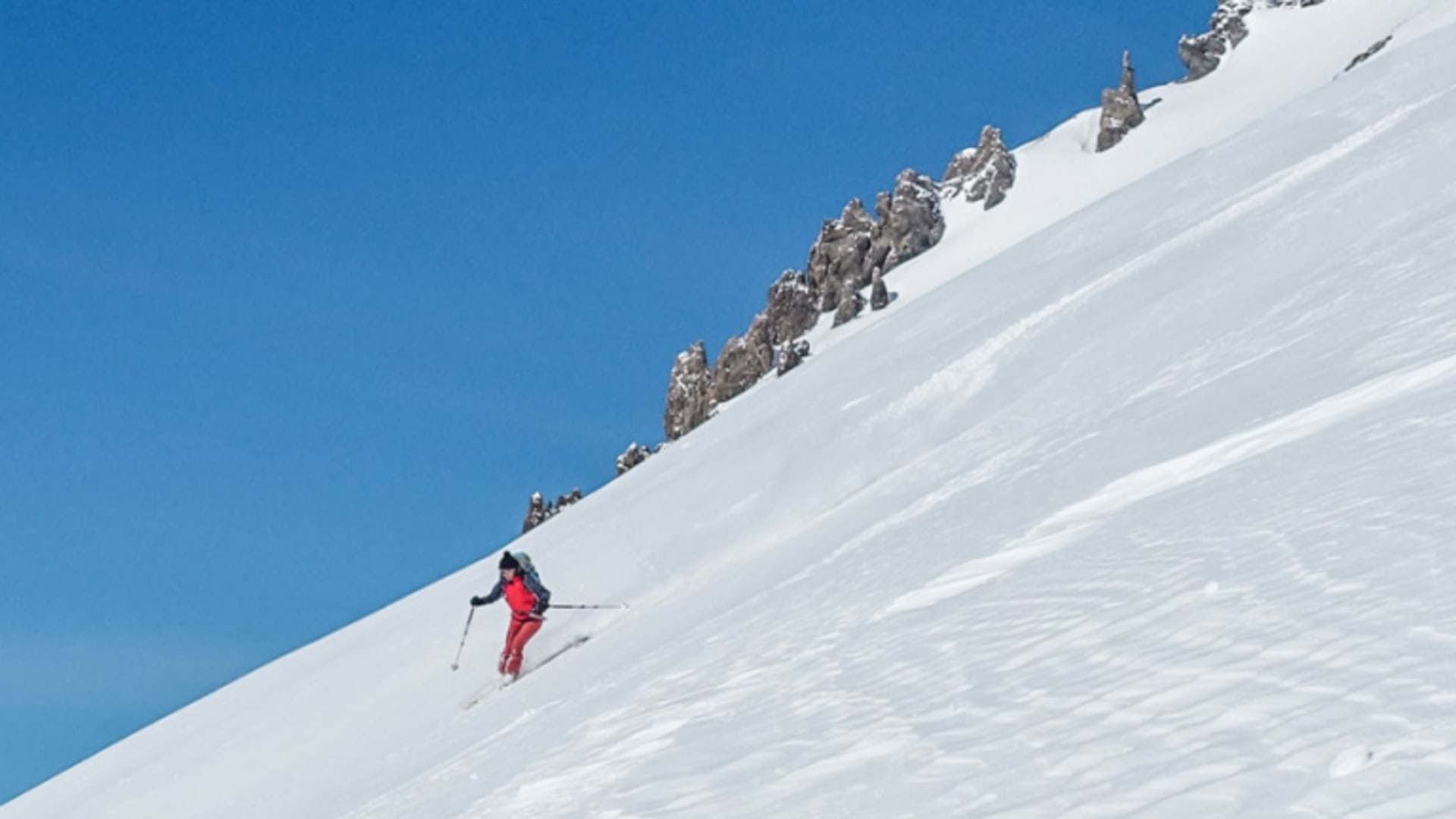 Skitourengeher in roter Jacke fährt einen unberührten Steilhang im Val Müstair auf Skiern ab.