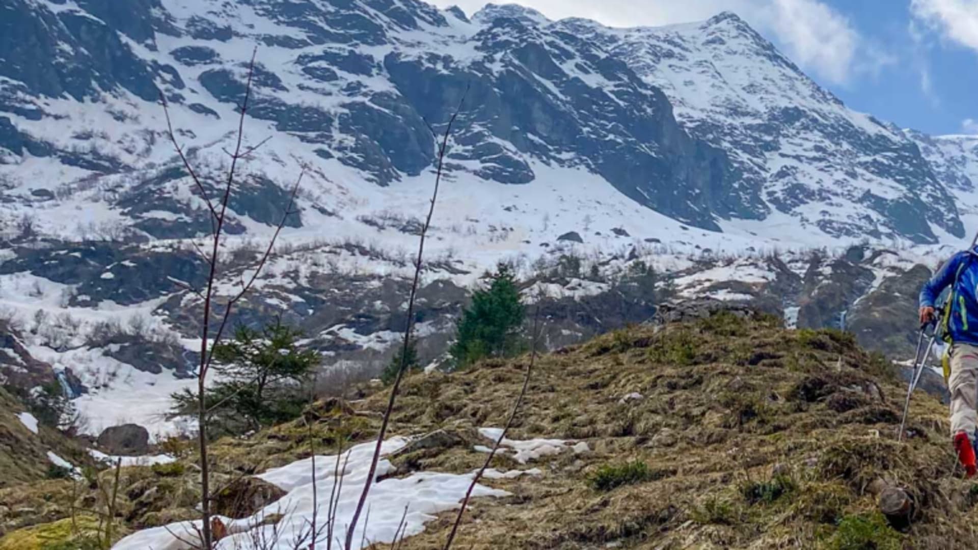 Skitourengeher mit Wanderstöcken und Rucksack steigt über grasigen Hang in den Urner Alpen auf.