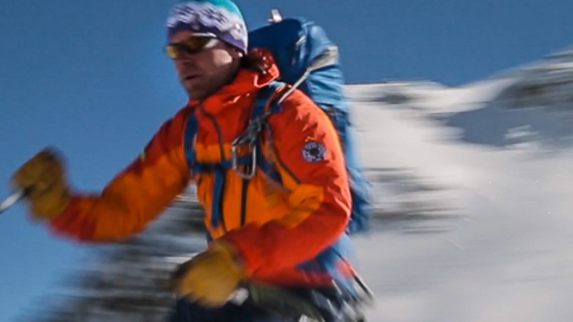 Skitourengeher in orangefarbener Jacke und blauem Rucksack beim steilen Aufstieg auf der Piz Buin Skitour