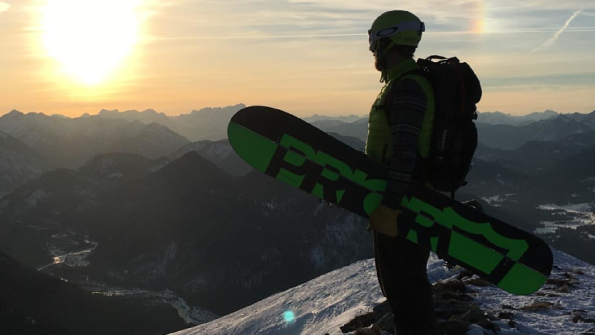 Freerider steht mit Splitboard auf schneebedecktem Berggrat im Wettersteingebirge bei Sonnenuntergang.