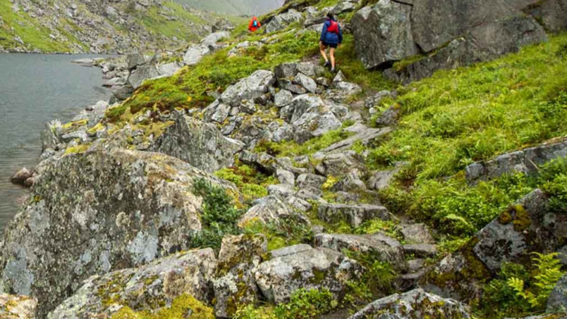 Trekking bei Tolmin: Zwei Wanderer mit Rucksäcken wandern entlang des felsigen Uferhangs eines Bergsees