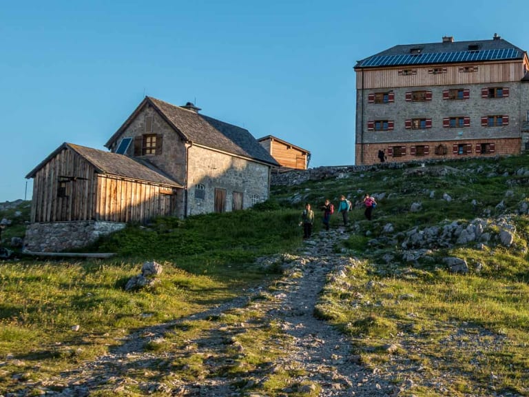 Drei Bergwanderer mit Rucksäcken gehen auf einem Pfad zum Watzmannhaus auf 1.930 m Höhe in den Berchtesgadener Alpen.