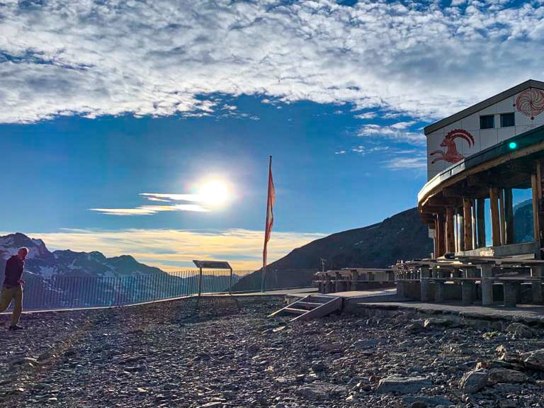 Das Berghaus Diavolezza steht auf einem Felsgrat mit Terrasse und Schweizer Flagge bei Sonnenschein.