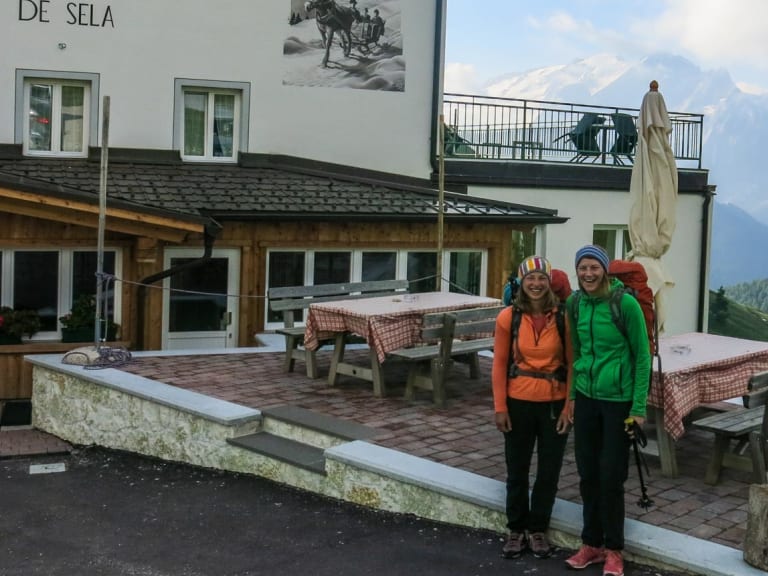 Zwei Bergwanderer mit Rucksäcken vor dem Rifugio Carlo Valentini am Sellajoch.