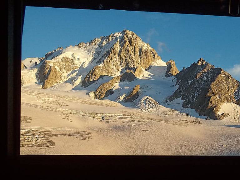 Blick durch das Panoramafenster des Refuge Albert 1er auf die verschneite Gletscherlandschaft des Hochgebirges.