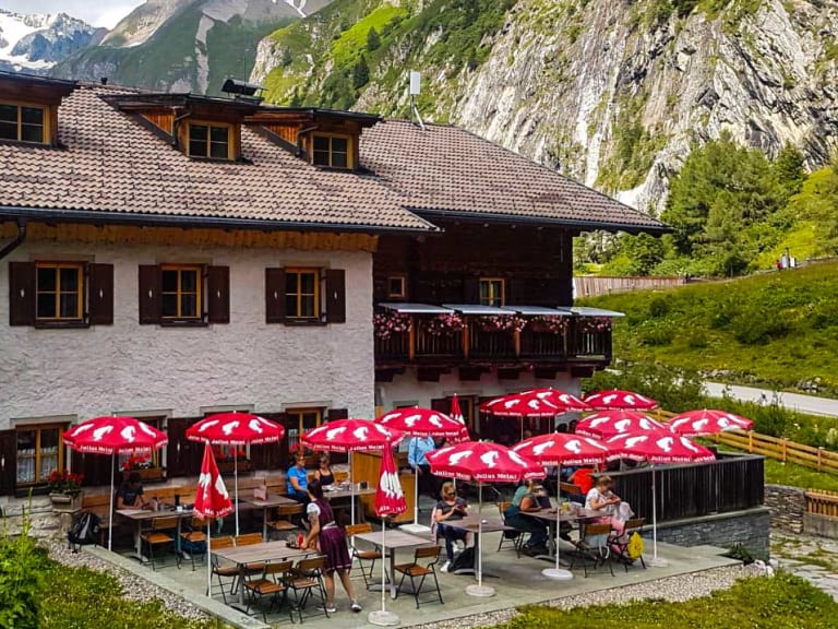 Gäste entspannen auf der Sonnenterrasse des Lucknerhaus mit roten Sonnenschirmen und Bergpanorama.