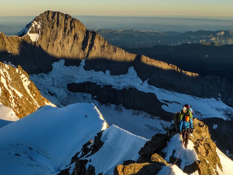 Zwei Bergsteiger klettern am schneebedeckten Felsgrat bei der Finsteraarhornhütte in den Berner Alpen bei Sonnenaufgang.