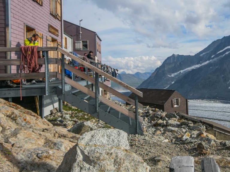 Bergsteiger vor der Konkordiahütte mit rosa-grauer Fassade direkt am Gletscherrand.
