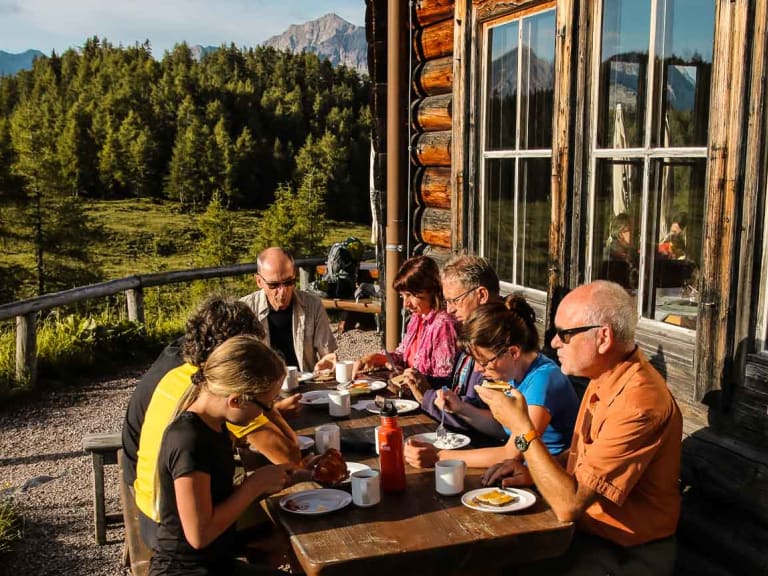 Wanderer beim Frühstück auf der Holzterrasse der Gotzenalm mit Blick auf die Berchtesgadener Alpen.