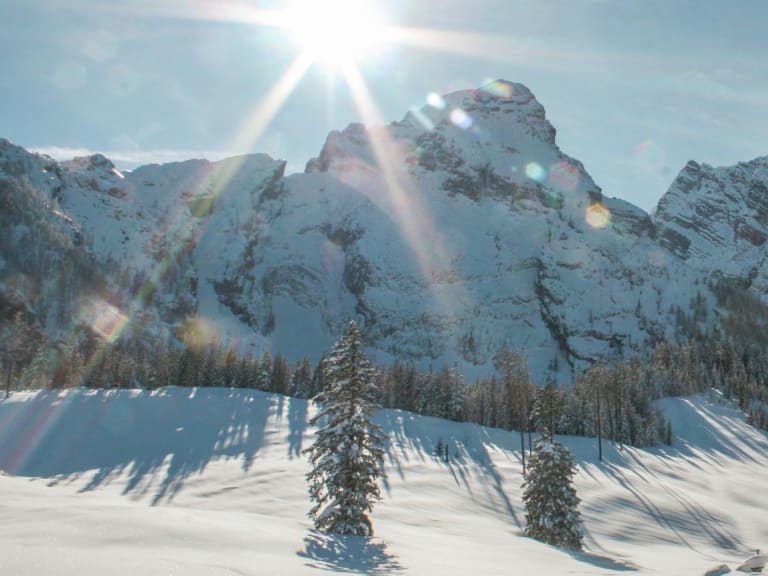 Die Kührointhütte liegt verschneit zwischen Fichten unter schneebedeckten Felsgipfeln bei Sonnenschein.