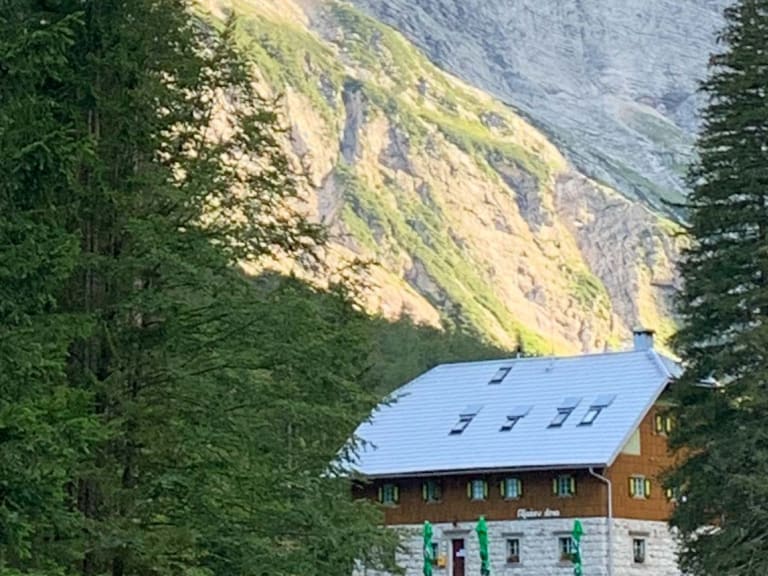 Bergsteiger vor dem Aljažev dom v Vratih mit traditioneller Bauweise aus Naturstein und Holz zwischen Fichten.