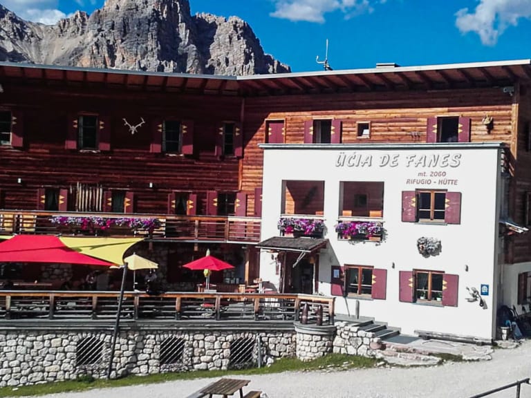 Die Faneshütte auf 2060 m zeigt traditionelle Alpenarchitektur mit Holzverkleidung, roten Fensterläden und violetten Blumenkästen vor steilen Felswänden.