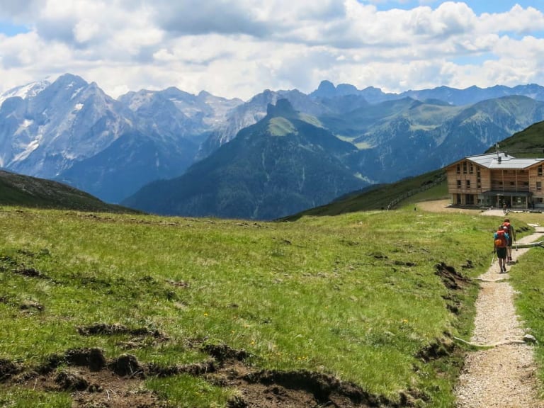 Zwei Wanderer mit Rucksäcken gehen auf Schotterweg zur Plattkofelhütte auf grünem Hochplateau.