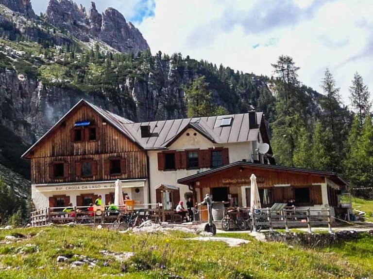 Das Rifugio Croda da Lago liegt auf grüner Almwiese mit großer Terrasse vor steiler Dolomiten-Felswand.