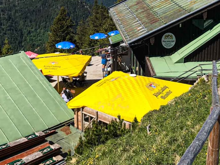 Panorama des Tegelberghaus mit Sonnenterrasse und Blick über die bewaldeten Täler der Ammergauer Alpen.