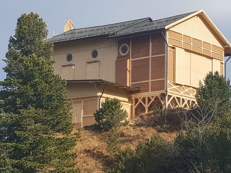 Das Schachenhaus zeigt seine charakteristische Holzfassade mit verglastem Wintergarten und Terrasse im dichten Bergwald.