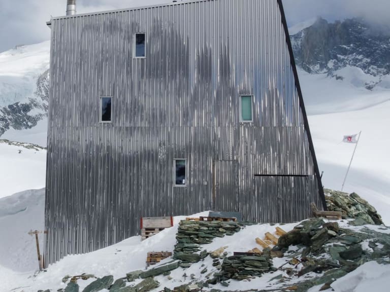 Die Cabane Tracuit steht auf felsigem Untergrund zwischen Schneefeldern und vergletscherten Gipfeln der Walliser Alpen.