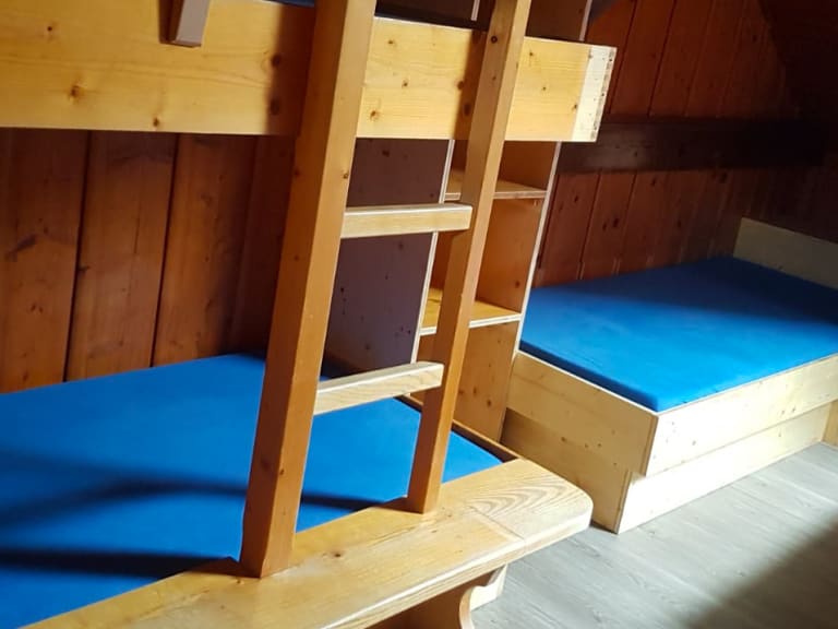 Schlafraum im Ingolstädter Haus mit Etagenbetten aus hellem Holz und blauer Bettwäsche an Holzwänden.