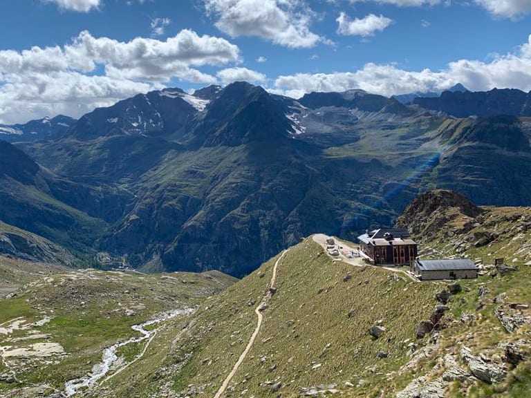 Luftaufnahme des Rifugio Chabod mit rechteckiger Architektur und Serpentinenpfad in karger Hochgebirgslandschaft.
