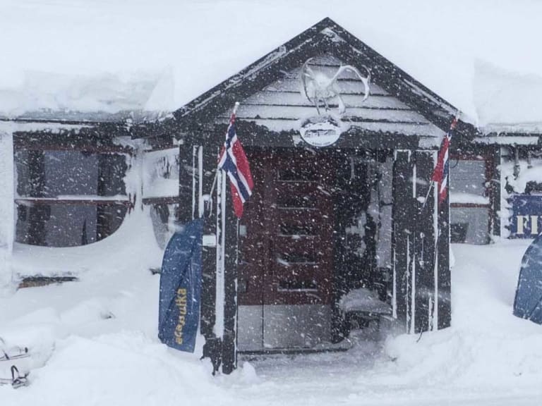 Das Hotel Finse 1222 bei starkem Schneefall mit schneeverdeckten Dächern und dem blauen Hotelschild davor.