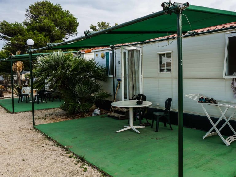 Mobilheim mit weißer Holzverkleidung und grünen Fensterläden im El Bahira Camping Village (San Vito lo Capo) mit überdac