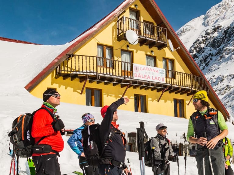 Fünf Skitourengeher stehen vor der gelben Cabana Bâlea Lac auf 2.034 m mit Skiausrüstung im Schnee der Südkarpaten.