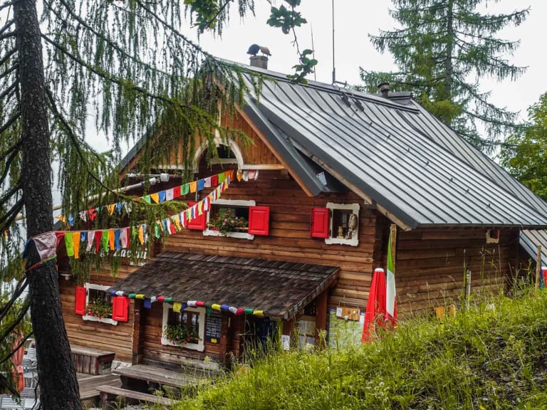 Das Rifugio Luigi Zacchi steht zwischen Fichten mit bunten Gebetsfahnen und roter Fensterläden auf 1.396 m Höhe.