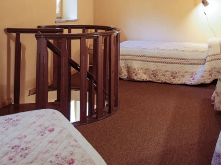 Mehrbettzimmer der Pensione Ceaglio mit vier Einzelbetten, weißer Bettwäsche und Holztreppe zum Obergeschoss.