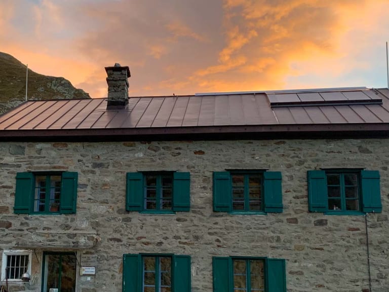 Das Rifugio Alfredo Rivetti zeigt sich als zweistöckiges Natursteingebäude mit grünen Fensterläden in den Walliser Alpen