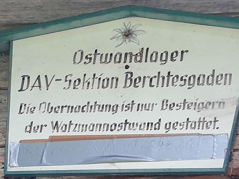 Hölzernes Hüttenschild des Ostwandlager der DAV-Sektion Berchtesgaden mit Edelweiß-Symbol.
