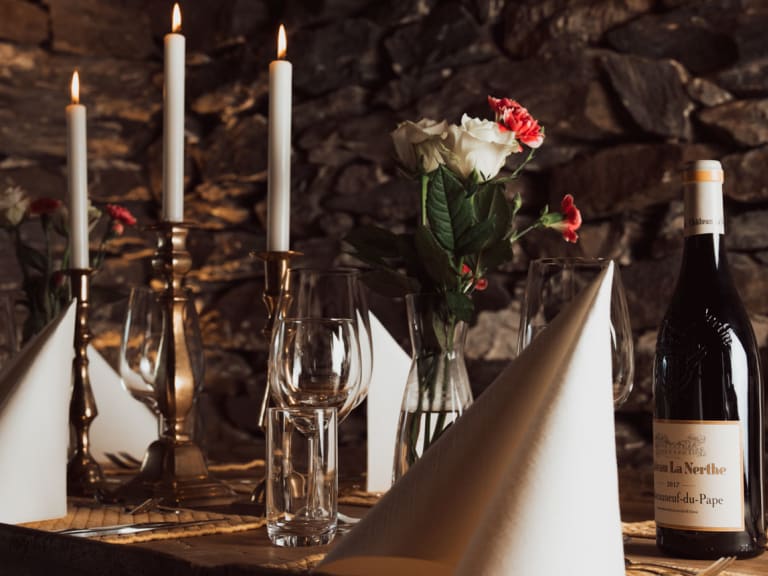 Elegant gedeckter Esstisch im Nes Gard Restaurant mit Kerzen, Rosen und Natursteinwand im Hintergrund.