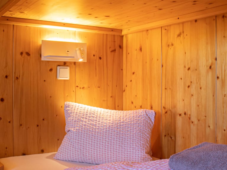 Schlafraum der Schihütte Zams mit komplett holzverkleideten Wänden und Einzelbett mit karierter Bettwäsche.