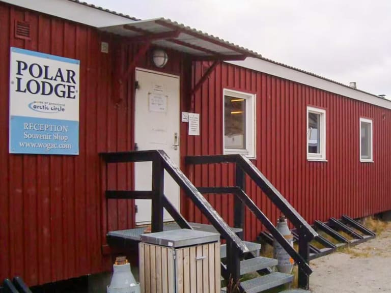 Außenansicht der Polar Lodge als langgestrecktes rotes Holzgebäude auf Stelzen mit weißen Fensterrahmen.