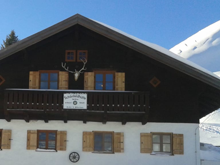 Die Schönfeldhütte zeigt sich im Winter mit verschneiter Alpenarchitektur und Hirschgeweih am Giebel.