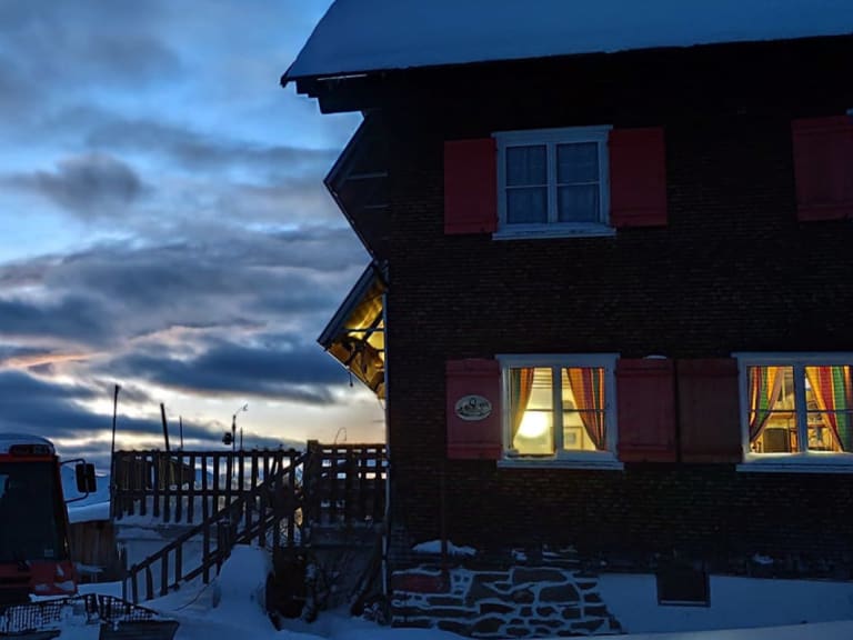 Winterliche Dämmerung am Neuhornbachhaus mit warm erleuchteten Fenstern und schneebedeckter Bergkulisse.