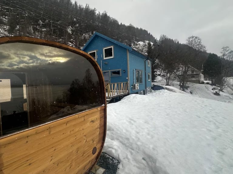 Außensauna mit Panoramafenster vor dem Lyngen Blue House in verschneiter Winterlandschaft.