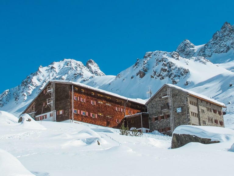 Skitourengeher vor der verschneiten Jamtalhütte in der Silvretta bei klarem Wetter.