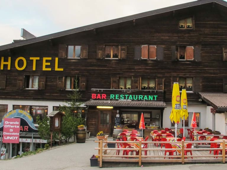 Das Hotel Bourg St Pierre zeigt seine traditionelle Holzfassade mit Restaurant-Terrasse und roten Gartenstühlen im Saint