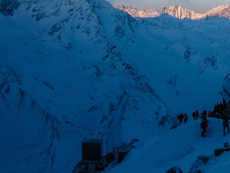 Die Cabane de Valsorey steht verschneit auf einem Felssockel während der blauen Stunde im Walliser Hochgebirge.