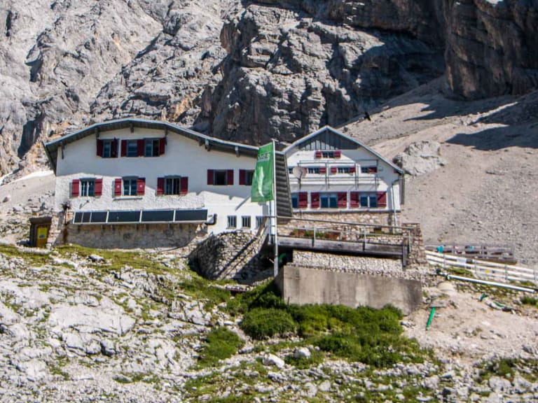 Gesamtansicht der Knorrhütte mit Haupt- und Nebengebäude vor den Felswänden des Zugspitzmassivs.