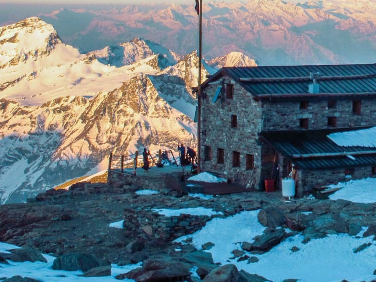 Mehrere Gebäudeteile des Rifugio Città di Mantova auf schneebedecktem Plateau während der Morgendämmerung.