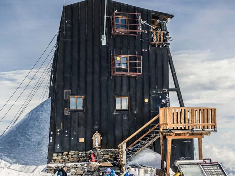 Bergsteiger in bunter Winterkleidung stehen vor der Capanna Margherita auf schneebedecktem Gipfel der Walliser Alpen.