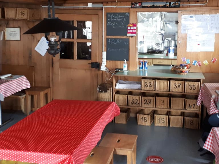 Gemütlicher Gastraum der Rothornhütte mit Holztischen, karierten Tischdecken und Bergsteigern bei der Einkehr.