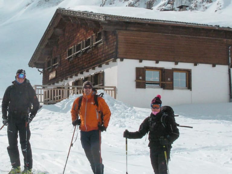 Drei Skitourengeher stehen vor der Sesvenna Hütte in verschneiter Hochgebirgslandschaft auf 2.262 m.