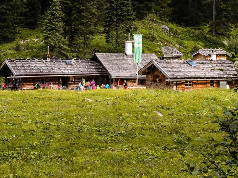 Die Wasseralm liegt auf einer grünen Bergwiese umgeben von Nadelwald im Nationalpark Berchtesgaden.