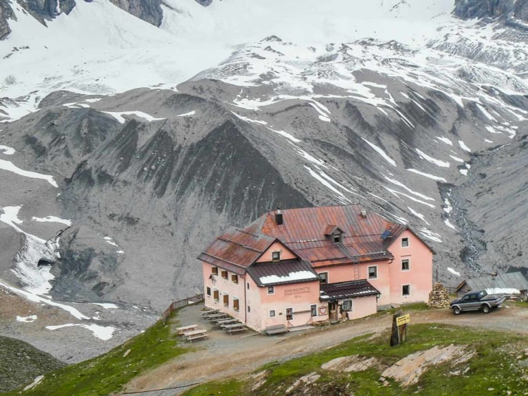 Die Schaubachhütte steht auf einem grünen Plateau vor schneebedeckten Berghängen im Ortlergebiet.