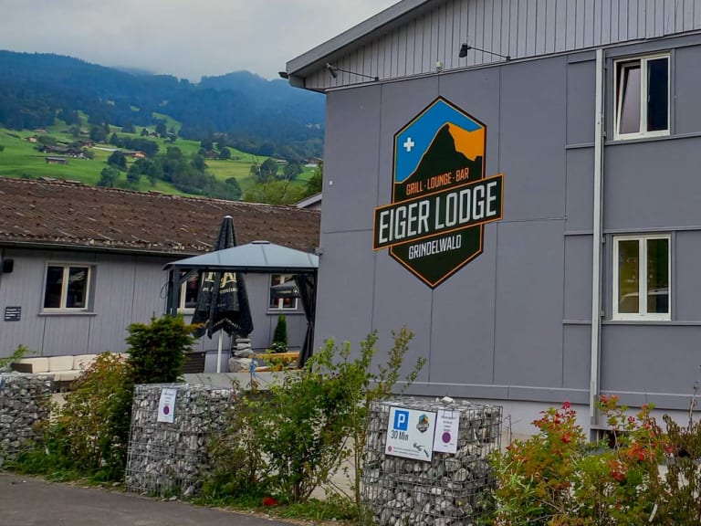 Das Hauptgebäude der Eiger Lodge zeigt eine graue Metallfassade mit großem Grindelwald-Logo an der Front.